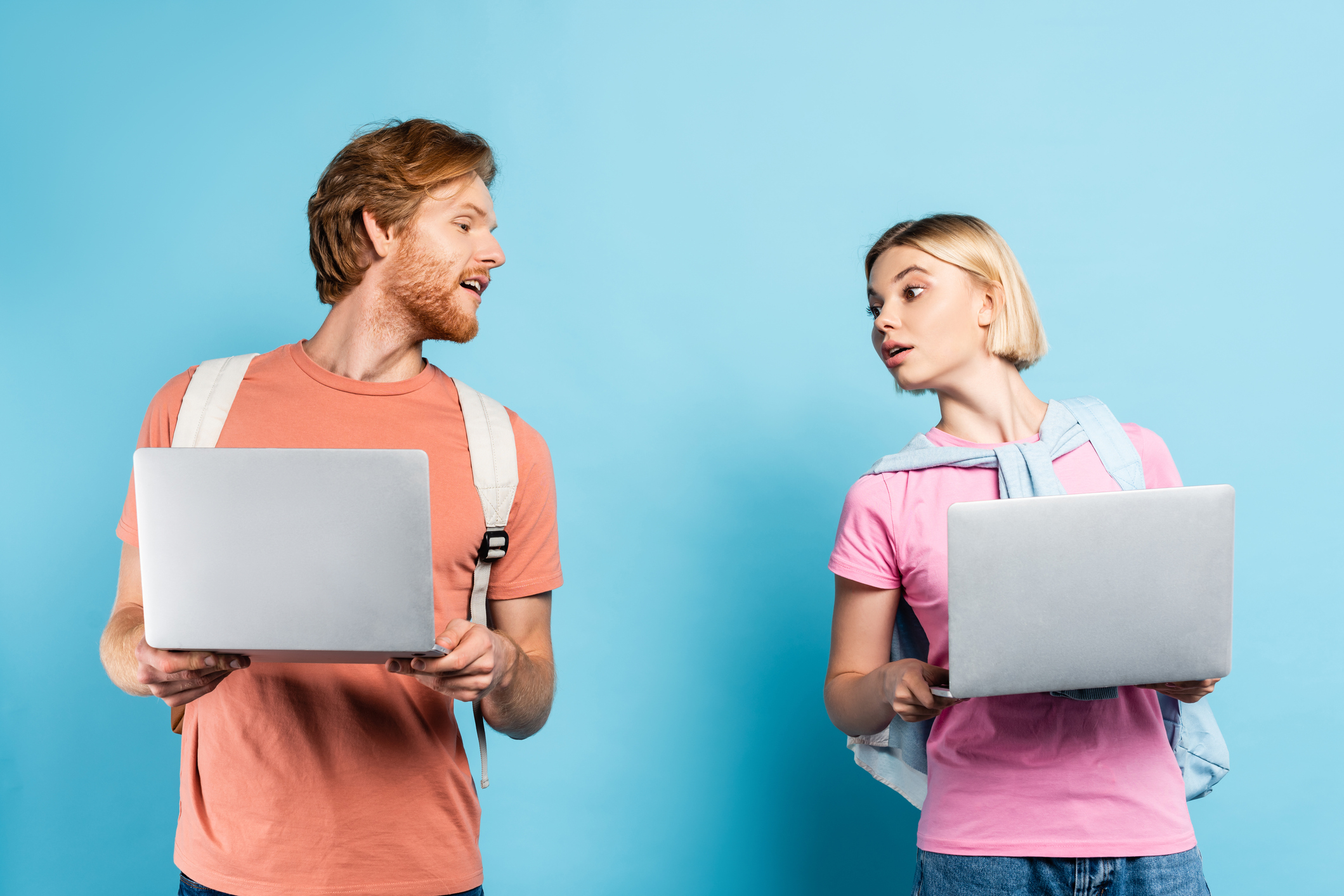 curious young students looking at each other laptops on blue